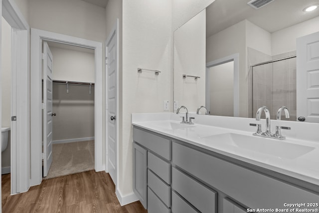 bathroom with a stall shower, wood finished floors, a walk in closet, and a sink