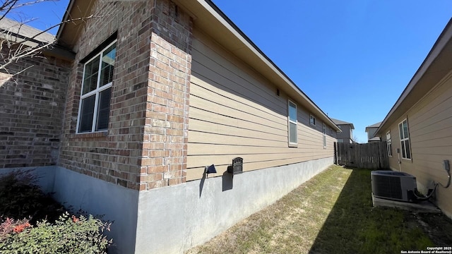 view of home's exterior featuring cooling unit, fence, brick siding, and a yard