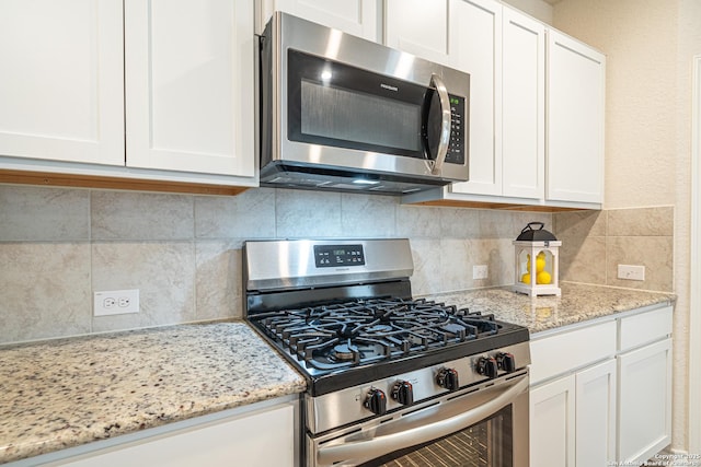 kitchen featuring decorative backsplash, white cabinets, stainless steel appliances, and light stone countertops