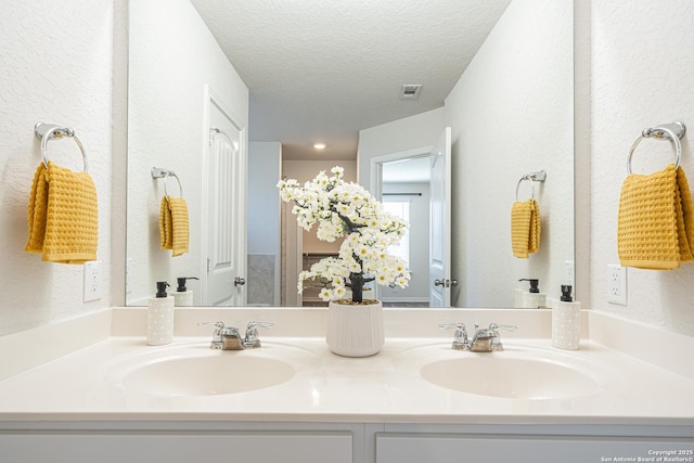 bathroom with a textured ceiling, double vanity, a textured wall, and a sink