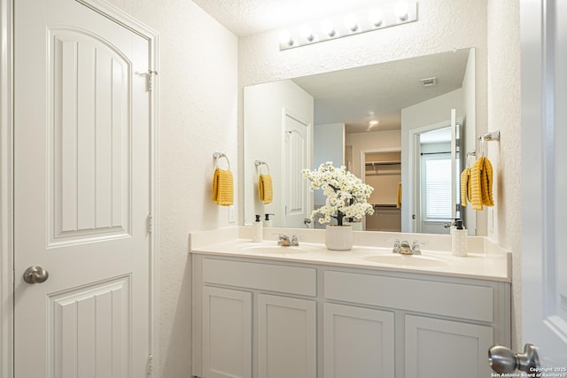 full bath with a textured ceiling, double vanity, and a sink