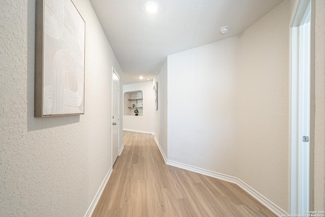 hallway with baseboards, light wood-style flooring, and a textured wall