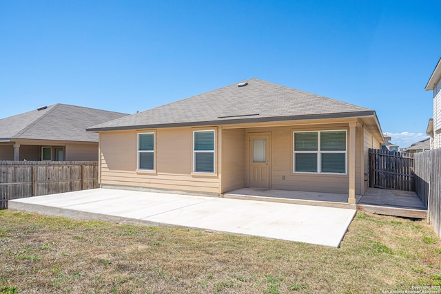 rear view of house featuring a patio, a fenced backyard, a lawn, and roof with shingles