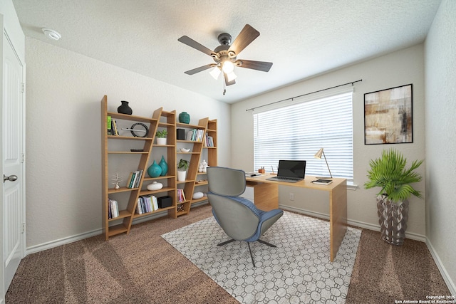 carpeted home office featuring baseboards, a textured ceiling, a ceiling fan, and a textured wall