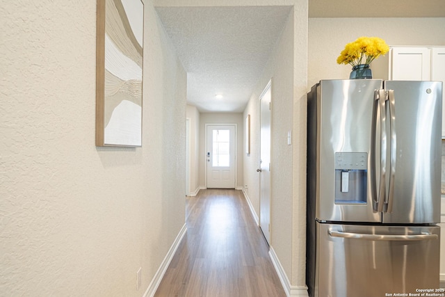 corridor featuring wood finished floors, baseboards, a textured wall, and a textured ceiling