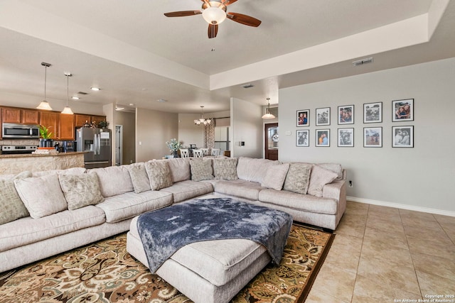 living area with visible vents, a raised ceiling, ceiling fan with notable chandelier, light tile patterned floors, and baseboards