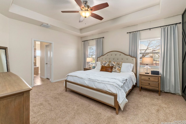 bedroom featuring visible vents, light carpet, a tray ceiling, ensuite bath, and baseboards