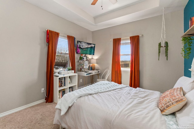 carpeted bedroom featuring a raised ceiling, a ceiling fan, and baseboards