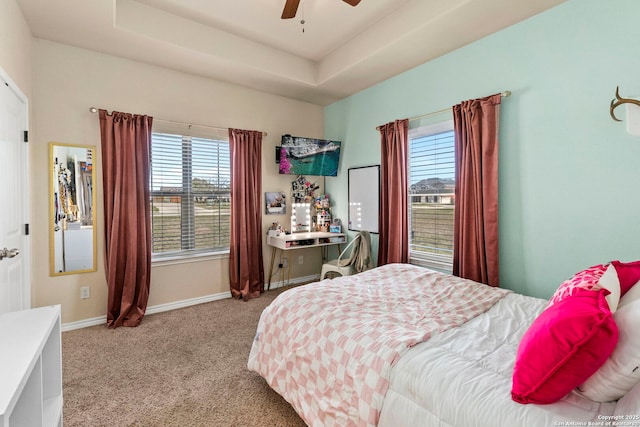 carpeted bedroom featuring a tray ceiling, a ceiling fan, and baseboards