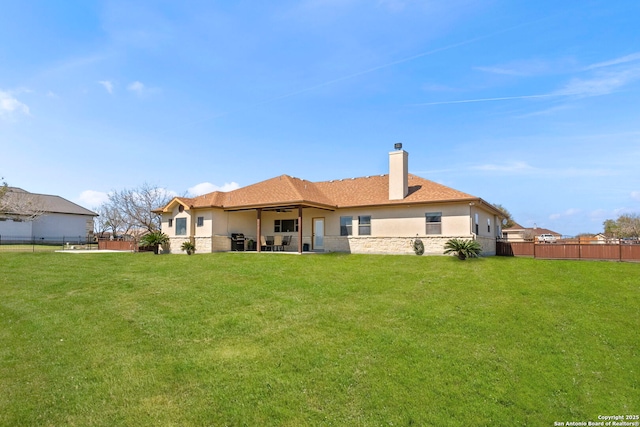 rear view of property featuring stucco siding, stone siding, fence, a yard, and a chimney