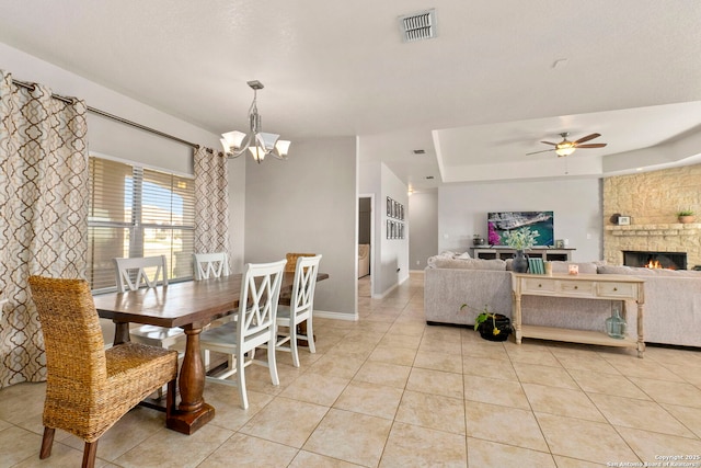 dining room with visible vents, baseboards, light tile patterned floors, a stone fireplace, and ceiling fan with notable chandelier