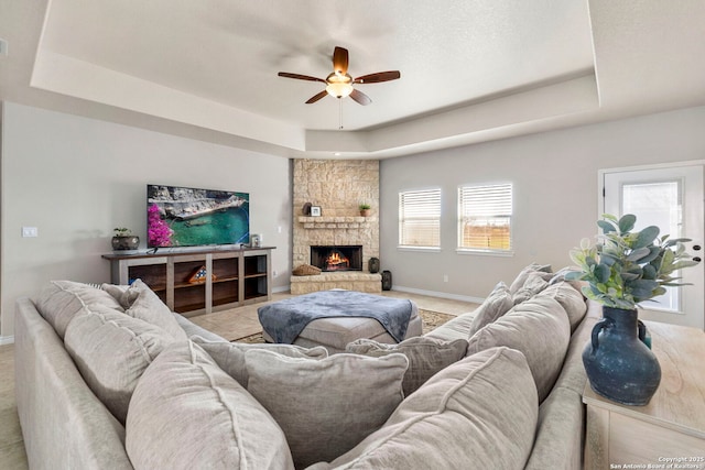 living area featuring ceiling fan, a fireplace, baseboards, and a tray ceiling