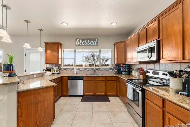 kitchen featuring light tile patterned floors, brown cabinets, a peninsula, stainless steel appliances, and a sink