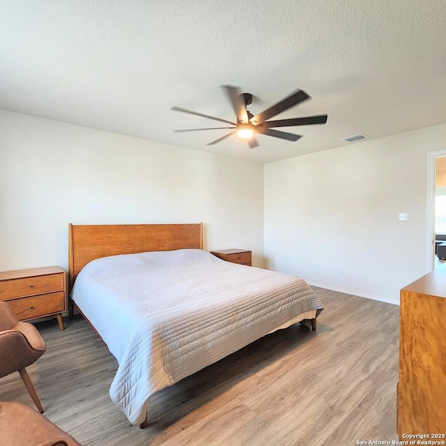 bedroom featuring visible vents, a ceiling fan, a textured ceiling, wood finished floors, and baseboards