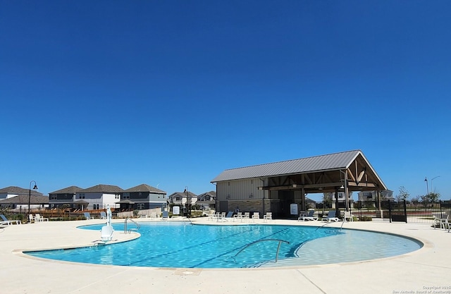 community pool with a patio area, fence, and a residential view