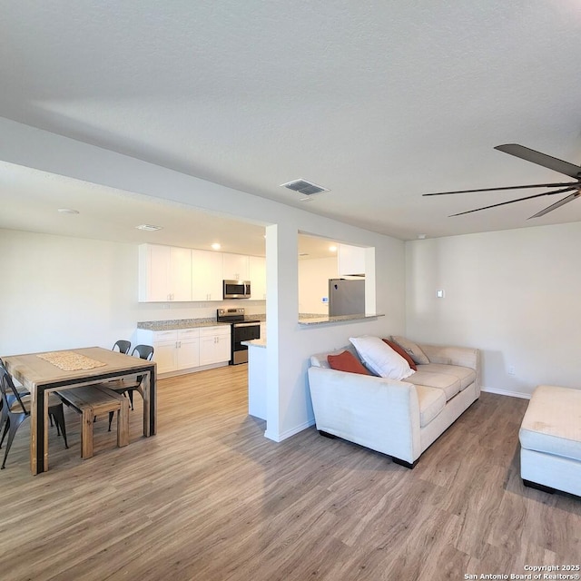 living room with light wood-type flooring, visible vents, baseboards, and a ceiling fan