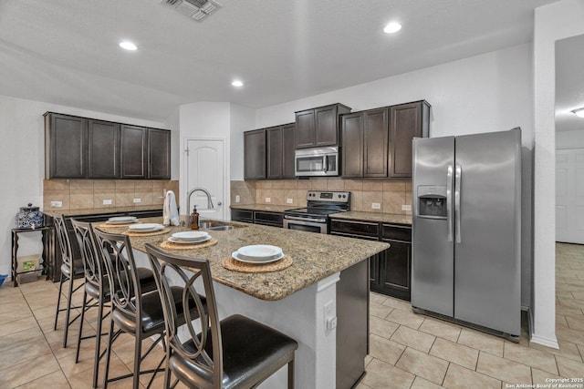 kitchen with visible vents, a kitchen bar, light stone counters, appliances with stainless steel finishes, and a sink