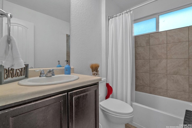 full bathroom featuring toilet, vanity, a textured wall, and shower / bath combo