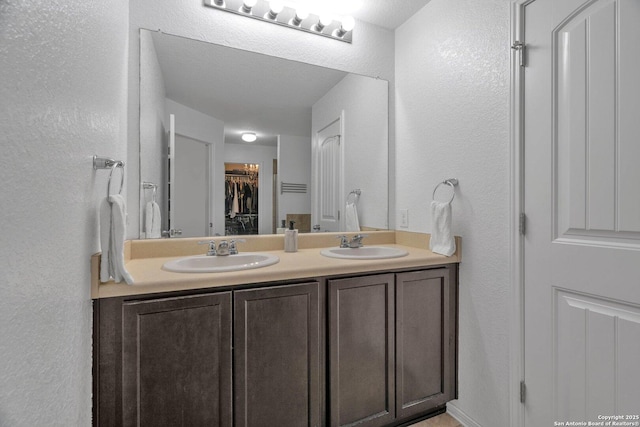 bathroom featuring a sink, a spacious closet, double vanity, and a textured wall