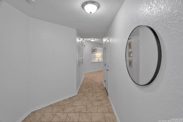 corridor with baseboards, a textured ceiling, and a textured wall