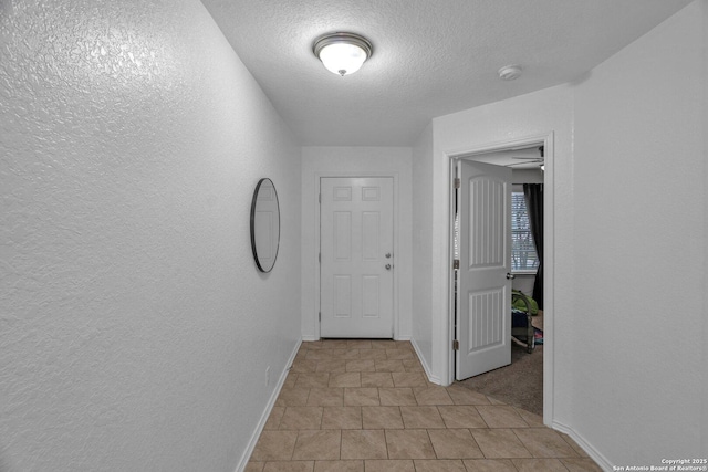 hallway featuring baseboards, a textured ceiling, and a textured wall