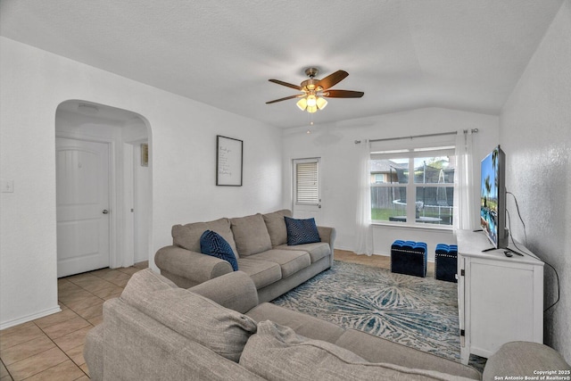 living area with a ceiling fan, arched walkways, light tile patterned flooring, baseboards, and vaulted ceiling