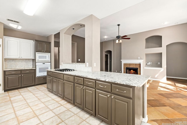 kitchen with visible vents, a tiled fireplace, backsplash, white appliances, and ceiling fan