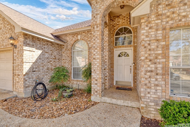 entrance to property featuring brick siding, a garage, and a shingled roof