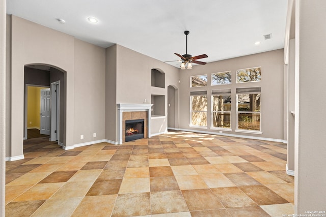 unfurnished living room with visible vents, baseboards, arched walkways, and ceiling fan