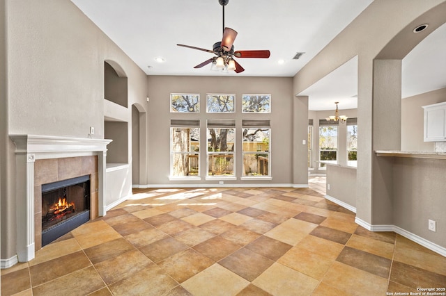 unfurnished living room featuring a tiled fireplace, ceiling fan with notable chandelier, baseboards, and visible vents