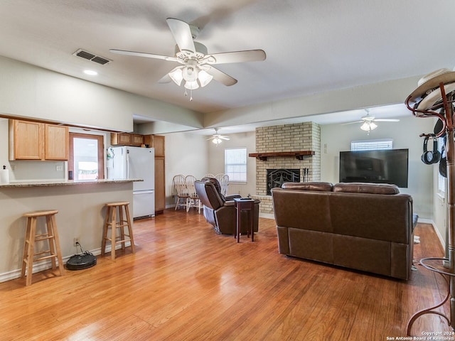 living room with ceiling fan, a fireplace, visible vents, and light wood-type flooring