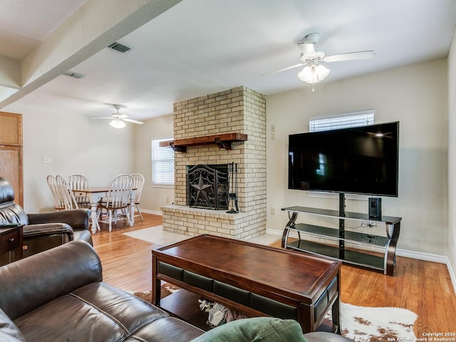 living room featuring baseboards, visible vents, ceiling fan, light wood-style floors, and a brick fireplace