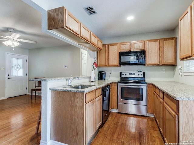 kitchen featuring visible vents, dark wood-type flooring, a peninsula, black appliances, and a sink