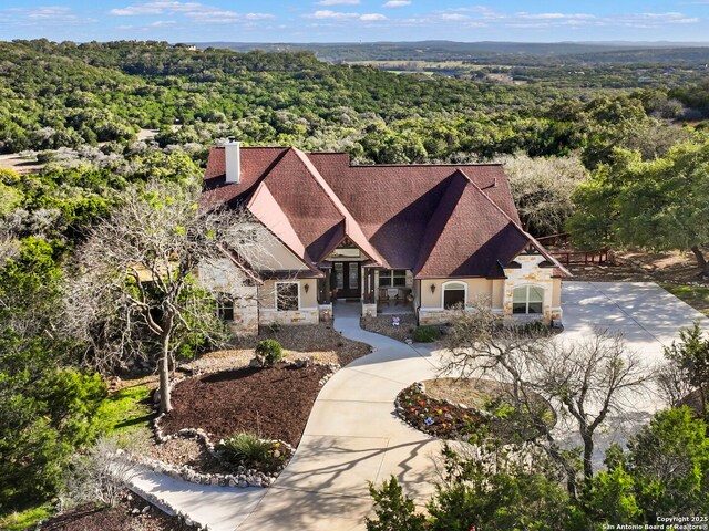 exterior space with a view of trees, stone siding, roof with shingles, and a chimney