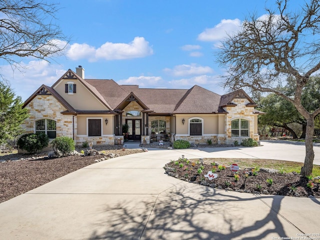 french provincial home with french doors, a chimney, driveway, and stucco siding