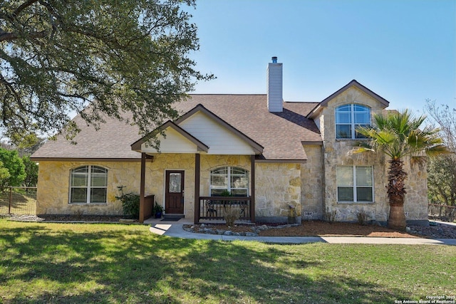 view of front of house with fence, roof with shingles, a chimney, a front lawn, and stone siding