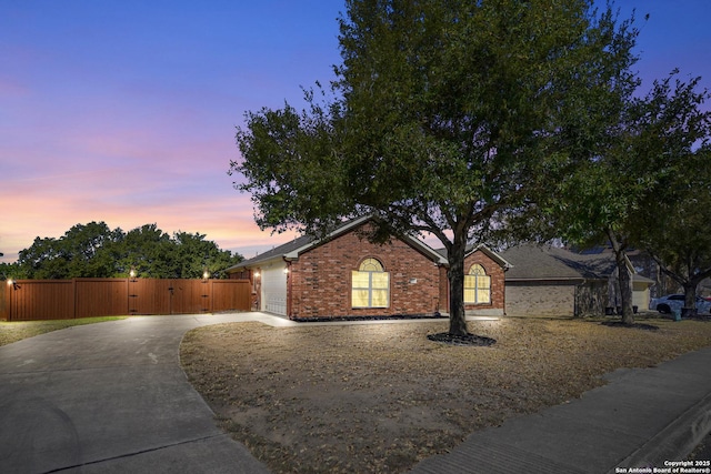 view of front of property with a gate, brick siding, concrete driveway, and fence