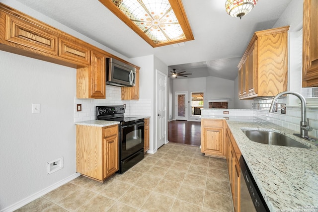 kitchen with light stone counters, a sink, stainless steel appliances, vaulted ceiling, and backsplash