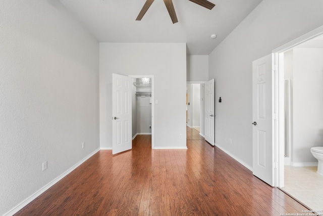 unfurnished bedroom with a walk in closet, baseboards, ensuite bath, and wood finished floors