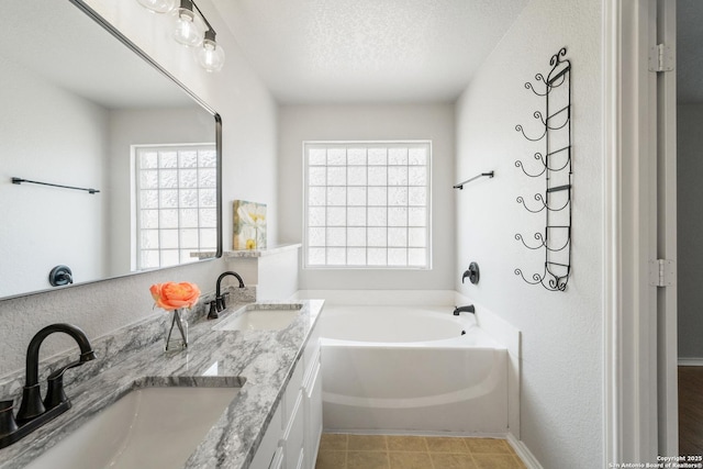 bathroom featuring a textured ceiling, double vanity, a bath, and a sink