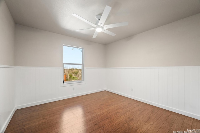 empty room featuring a ceiling fan, wood finished floors, and a wainscoted wall