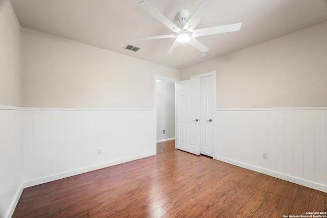 unfurnished room featuring visible vents, a wainscoted wall, wood finished floors, and a ceiling fan