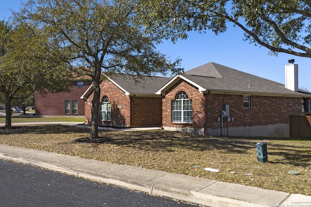 ranch-style home with a front lawn, brick siding, roof with shingles, and a chimney