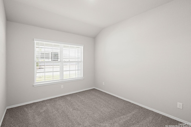 carpeted spare room featuring vaulted ceiling and baseboards