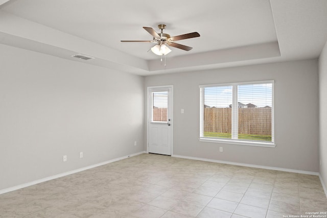 empty room with a tray ceiling, baseboards, visible vents, and ceiling fan