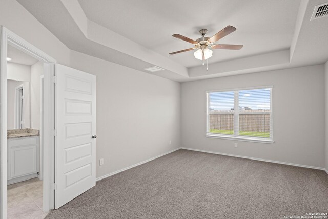 unfurnished room featuring visible vents, a raised ceiling, light colored carpet, and baseboards