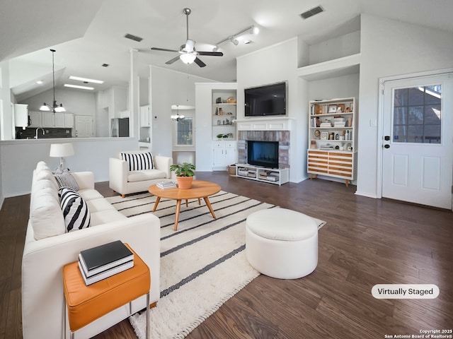 living area with a fireplace, lofted ceiling, wood finished floors, and visible vents