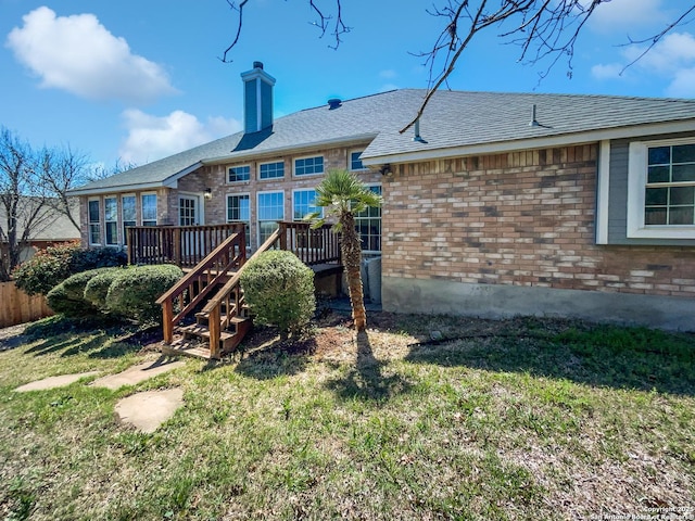 back of property featuring a deck, a yard, a shingled roof, brick siding, and a chimney