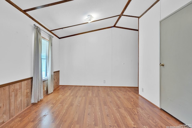 unfurnished room with a wainscoted wall, wood walls, lofted ceiling, ornamental molding, and light wood-style floors