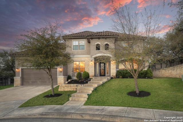 mediterranean / spanish-style home with driveway, an attached garage, a yard, stucco siding, and stone siding